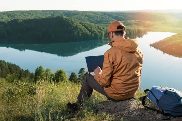 istock Remote work concept. Man sitting alone in nature wilderness working on laptop. 1324516635