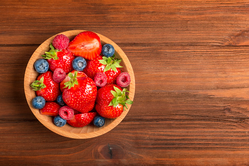 Raspberries, Strawberries and Blueberries in wooden Bowl on rustic Wooden Table. Healthy Food Concept. Top View Background