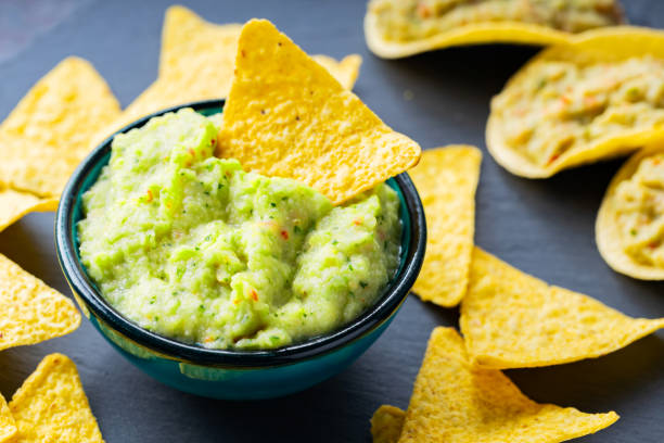 istock Guacamole and nachos chips on a dark background. Guacamole sauce with corn chips on a slate board. Close-up. Selective focus 1324535585