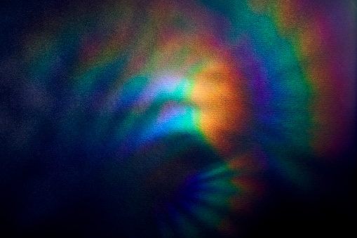 Bright multicolored glare on dark rough textured cardboard. Soft rainbow light. Abstract colorful background.