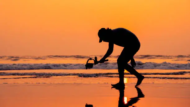 Photo of A young and independent filmmaker filming near beach silhouette