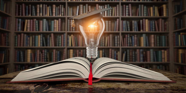 istock Education, knowledge and innovation concept background. Light bulb with mortar board on open book in vintage library. 1324547826