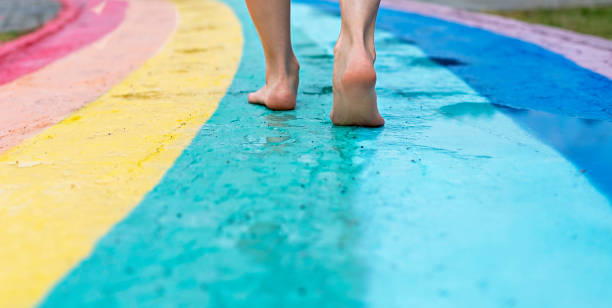женские �ноги крупным планом на босиком по мокрому асфальту обращается радуга пешеходная дорожка после дождя среди луж, копировать простра� - human leg women shower water стоковые фото и изображения