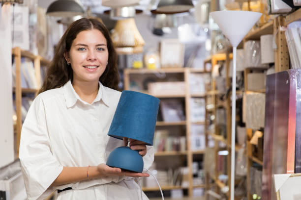 istock Young woman choosing table lamp at store 1324553538