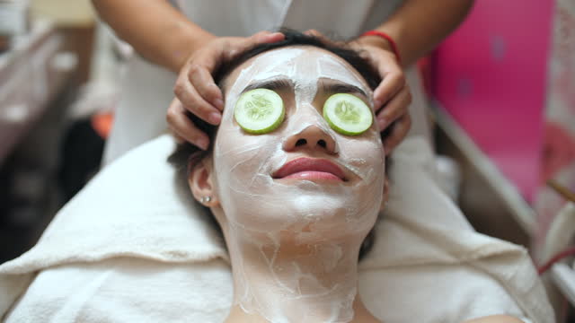 Beautiful young woman gets a face mask in the spa center, lying with cucumbers in her eyes