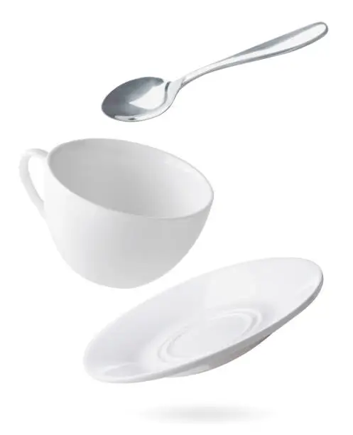 Photo of Empty dishes cup, plate and spoon are flying on a white. Isolated