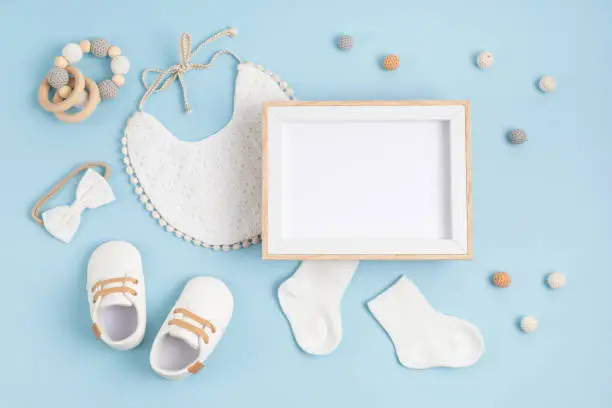 Mockup of empty frame with white baby accessories. Baby shower, baptism invitation, greeting card. Template for brand, logo, advertising. Flat lay, top view