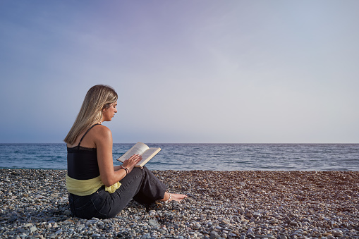 Pretty young woman reading a book on the beach