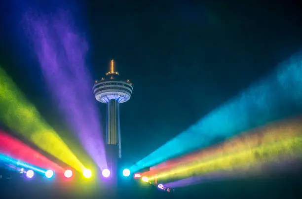 Niagara Falls City tower surrounded with beams of colourful lights at night on the Canadian side