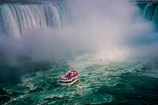 Horseshoe Falls and a tourist ferry boat from underneath the Niagara Falls, surrounded with massive waterfalls, Ontario, Canada