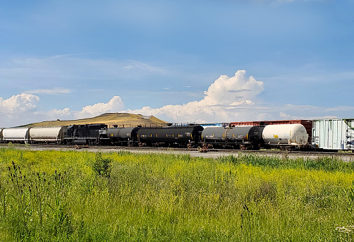 Freight train with blue sky and clouds and landfill in the background and green grass in the foreground - taken near Fostoria, Ohio, USA