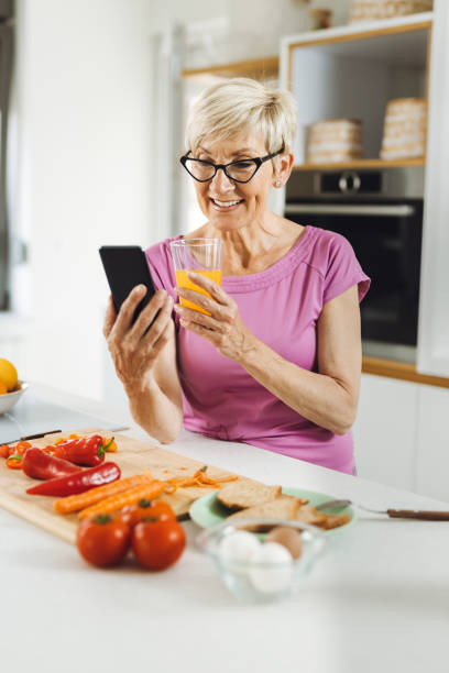 istock Happy senior  woman using cell phone during breakfast time in the kitchen 1324573897