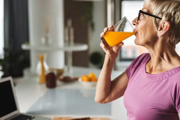 Profile view of a senior woman drinking fresh juice in the kitchen