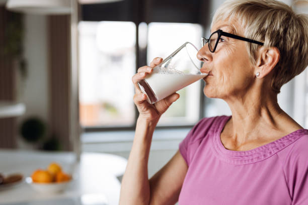 reife frau trinken frische milch aus einem glas - milch stock-fotos und bilder