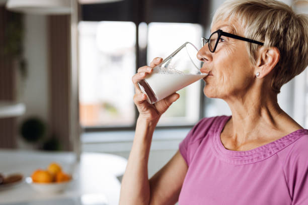 mujer madura bebiendo leche fresca de un vaso - dairy products fotos fotografías e imágenes de stock