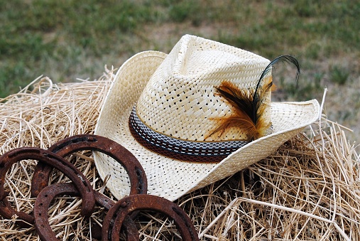 Sombrero de vaquero occidental junto a cuatro zapatos de caballo oxidados en una pila de heno de paja photo