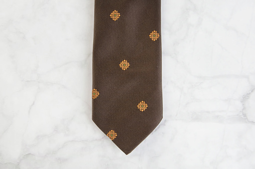 Brown neck tie with geometric pattern on marble background. Copy space for text.
