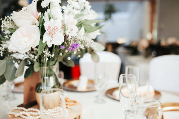 istock Modern wedding decor - guest tables with white tablecloths, golden plates, white roses and eucalyptus leaves floral arrangements. 1324581945