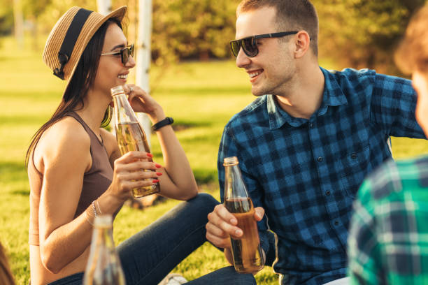istock young woman in a summer hat and sunglasses communicates with a young man drinking drinks on a picnic in the park 1324593575