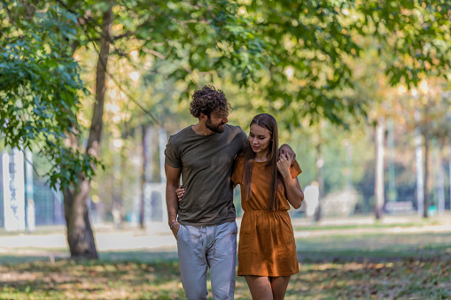 A Young Woman and her Husband are Walking in Park, and Embracing While Having a Romantic Talk.