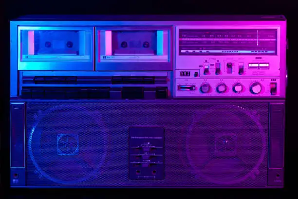 Vintage portable stereo boombox cassette recorder from 80s with reflection of blue and pink neon light.