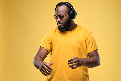 African-american ethnicity person at the studio with professional wireless black headphones is listening music. Concept for dj, pop, rap, r&b music photography. Portrait on yellow background