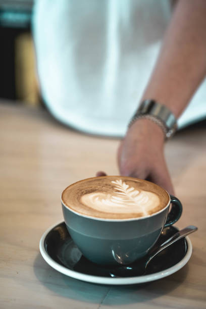 istock Barista offering latte with decorative leaf on foam milk 1324605388