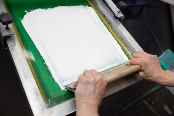 istock Serigraphy silk screen print process at clothes factory. Frame, squeegee and plastisol color paints 1324605643