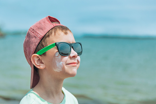 happy kid wearing sunglasses and sunscreen on his face. copy space for your text