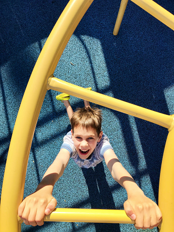 Young boy hanging on the yellow bars by his hands.  top view