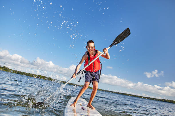glücklicher junge paddeln auf stand up paddle board. - life jacket stock-fotos und bilder