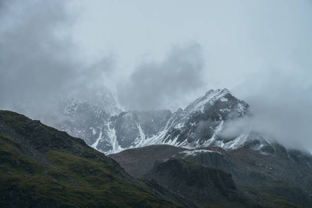 istock Atmospheric alpine landscape with great mountain peaked top with snow in low clouds. Dramatic mountain scenery with sharp pinnacle in overcast weather. Awesome view to snowy pointy peak in cloudy sky. 1324608564