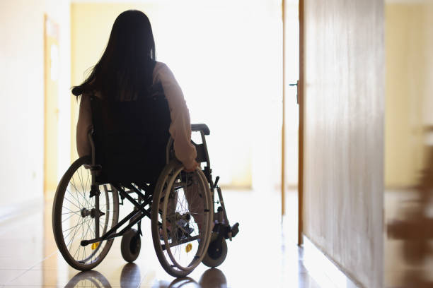 donna in sedia a rotelle in corridoio buio guarda fuori dal finestrino - disablement foto e immagini stock