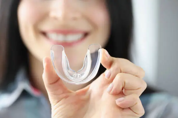 Photo of Smiling woman holds transparent plastic mouth guard in her hand