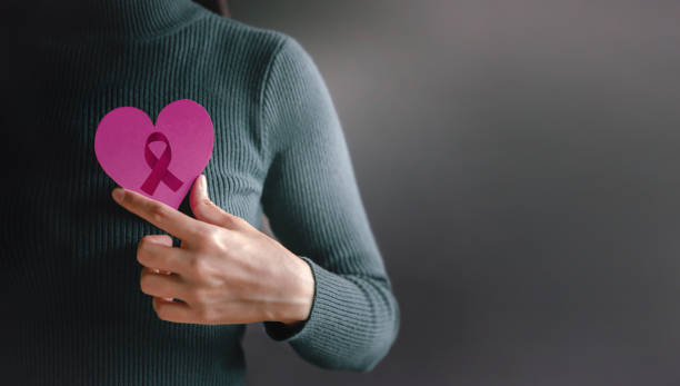 Love, Health Care, Donation and Charity Concept. Breast Cancer Awareness. World Cancer Survivor Day Love, Health Care, Donation and Charity Concept. Breast Cancer Awareness. World Cancer Survivor Day. Close up of Woman Holding a Heart with Ribbon on her Breast breast cancer stock pictures, royalty-free photos & images