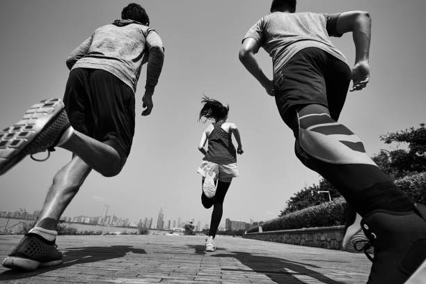 rear view of three asian runners running in seaside park three young asian adults running jogging outdoors, rear and low angle view, black and white chasing photos stock pictures, royalty-free photos & images
