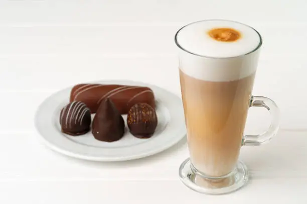 Cup of coffee and saucer with chocolate sweets on wooden table close up