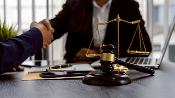 istock Lawyers shake hands with clients to work on contract documents and hammer with scales and laptops on a courtroom table. Judiciary concept 1324625412