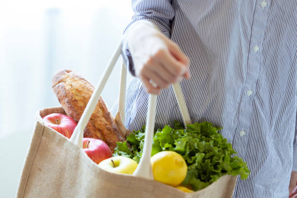 Hand of a woman with vegetables and bread with eco bag Hand of a woman with vegetables and bread with eco bag reusable bag stock pictures, royalty-free photos & images