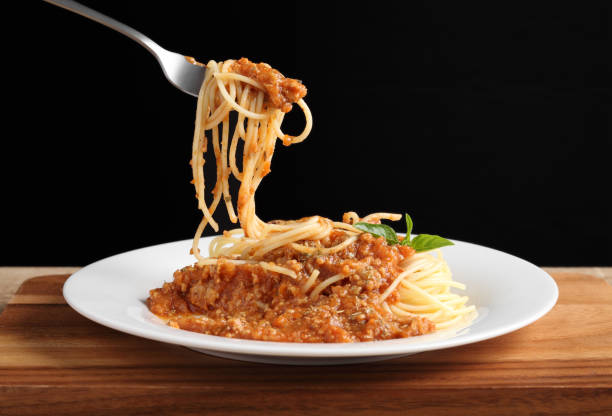 istock Hand holding a fork with spaghetti and red sauce in white dish on wooden cutting board 1324628085