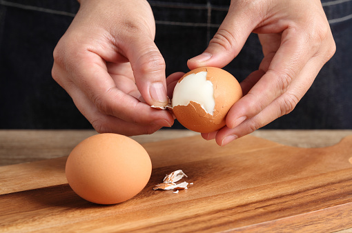 Chef peeling boiled egg on wooden cutting board in kitchen
