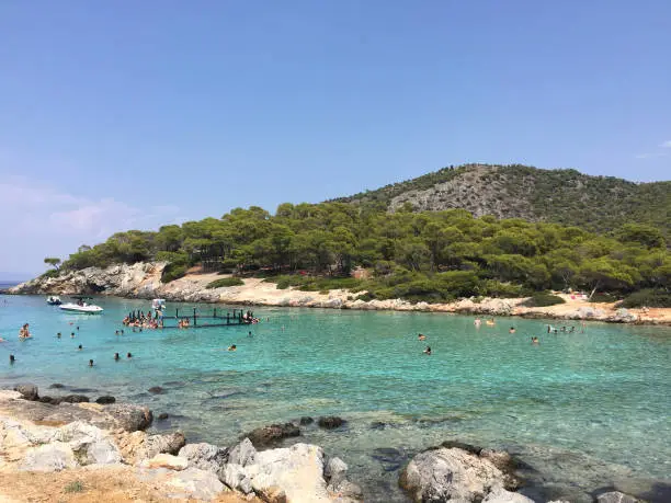 Photo of Aponisos beach, a pebble beach in a small cove with sheltered swimming, seen from Aponisos island in the vicinity of Agistri, Greece.