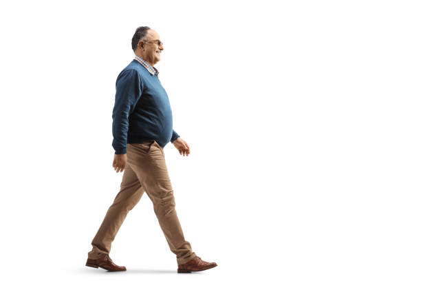 full length profile shot of a casual mature man smiling and walking - lopen stockfoto's en -beelden
