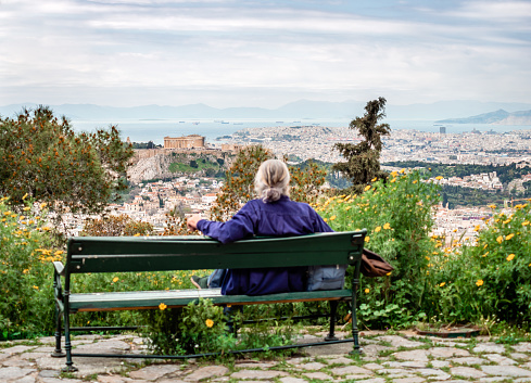 Athens, Greece - April 4 2015: Rear view of a defocused unidentified seated man enjoying the view from Lycabettus Hill. The Acropolis dominates the picture, while the Saronic gulf and the city and port of Piraeus are in the background.