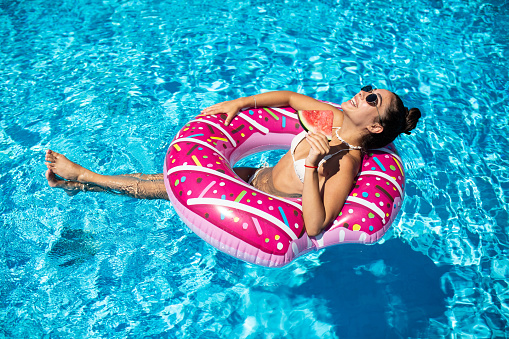Beautiful, attractive woman enjoys the pool in an inflatable donut and holds watermelons
