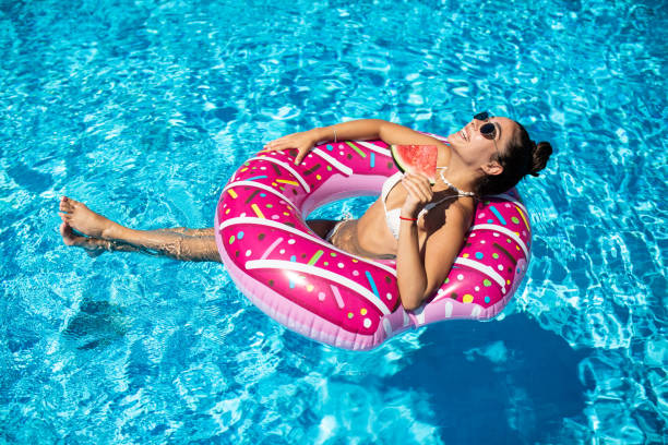 mulher bonita e atraente curte a piscina em um donut inflável e segura melancias - above ground pool - fotografias e filmes do acervo