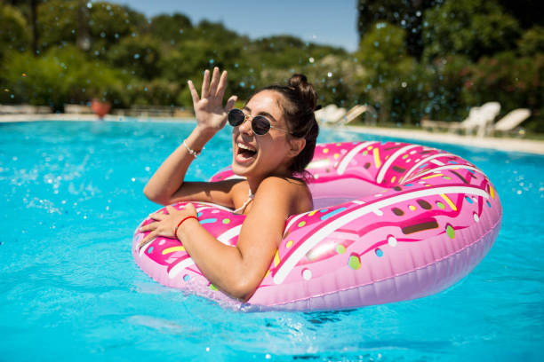 una hermosa chica en la piscina en un donut inflable se divierte en un caluroso día de verano - diversión fotografías e imágenes de stock