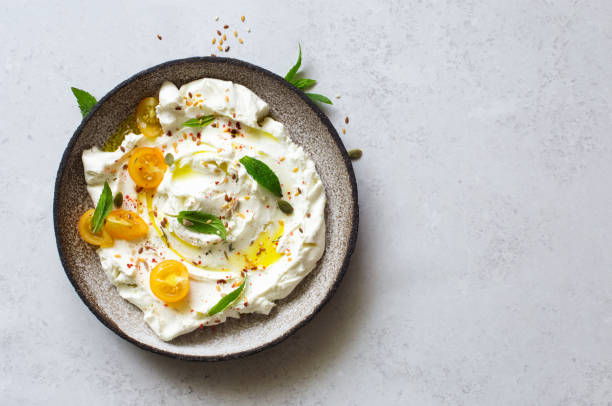 Homemade yogurt soft cheese (labneh) with yellow cherry tomatoes and seeds on rustic plate. Flat lay. Copy space Homemade yogurt soft cheese (labneh) with yellow cherry tomatoes and seeds on rustic plate. Flat lay. Copy space dipping sauce stock pictures, royalty-free photos & images