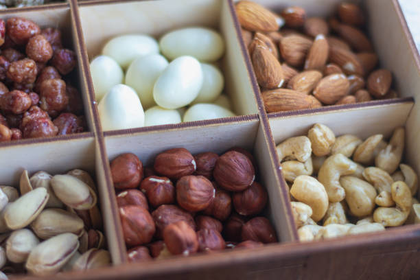 Many different types of nuts in a wooden box: hazelnuts, peanuts, pistachios, almonds, macadamia, cashews.