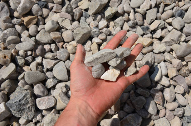 homem segura em sua mão uma amostra de cascalho de pedra ou pedras de um tamanho. cascalho branco de mármore e pedras marrons cinzas direto da pedreira. - media mixed - fotografias e filmes do acervo